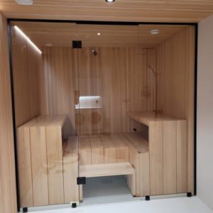 Kirkas saunan lasiseinä Kirkkonummella, kokolasiovi ja kaksi kiinteää lasia mustilla saranoilla ja heloilla